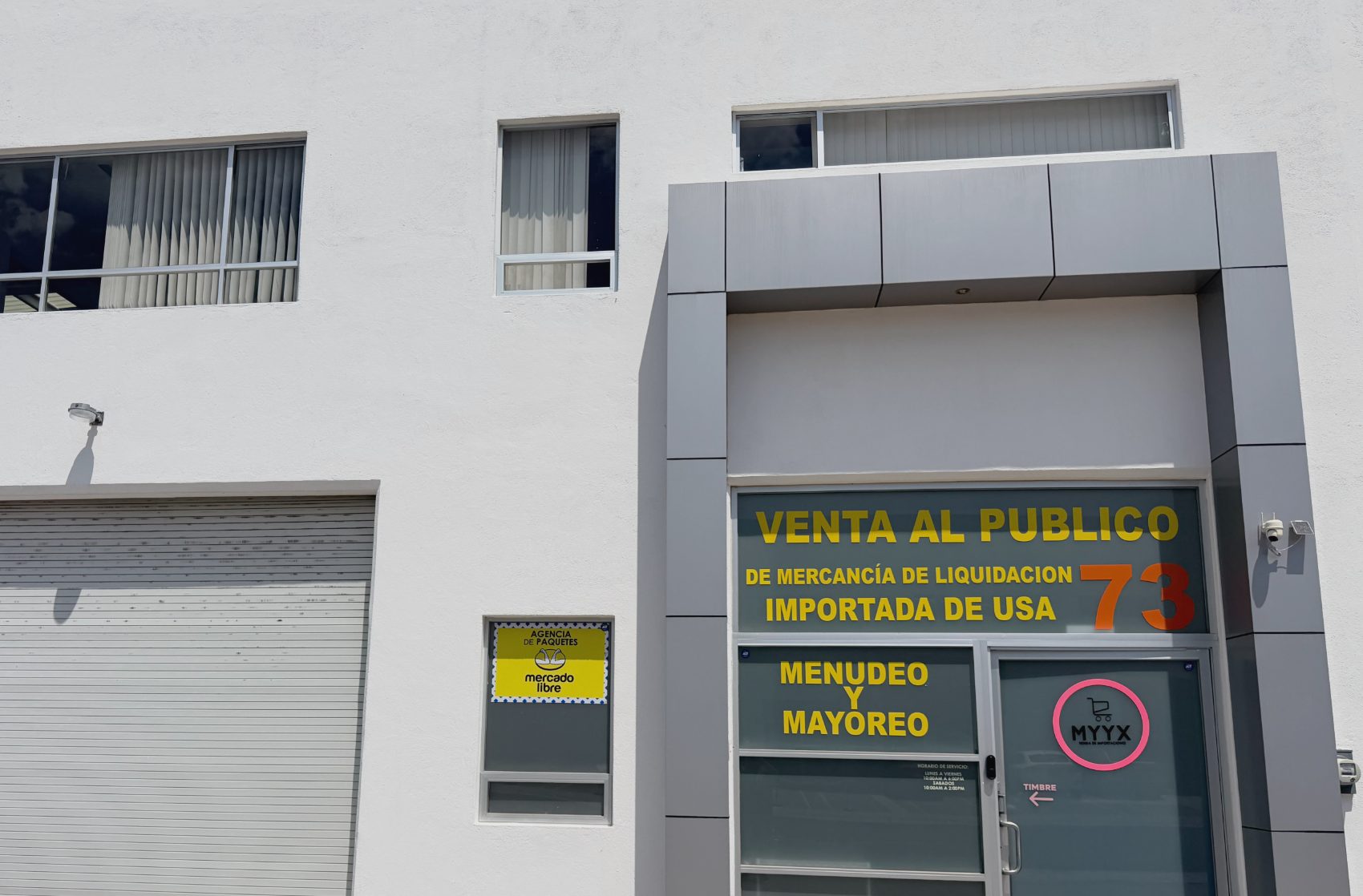 Fachada de MYYX en el parque industrial: acceso de la bodega 73 con el letrero de venta al público de mercancía de liquidación importada de USA, menudeo y mayoreo