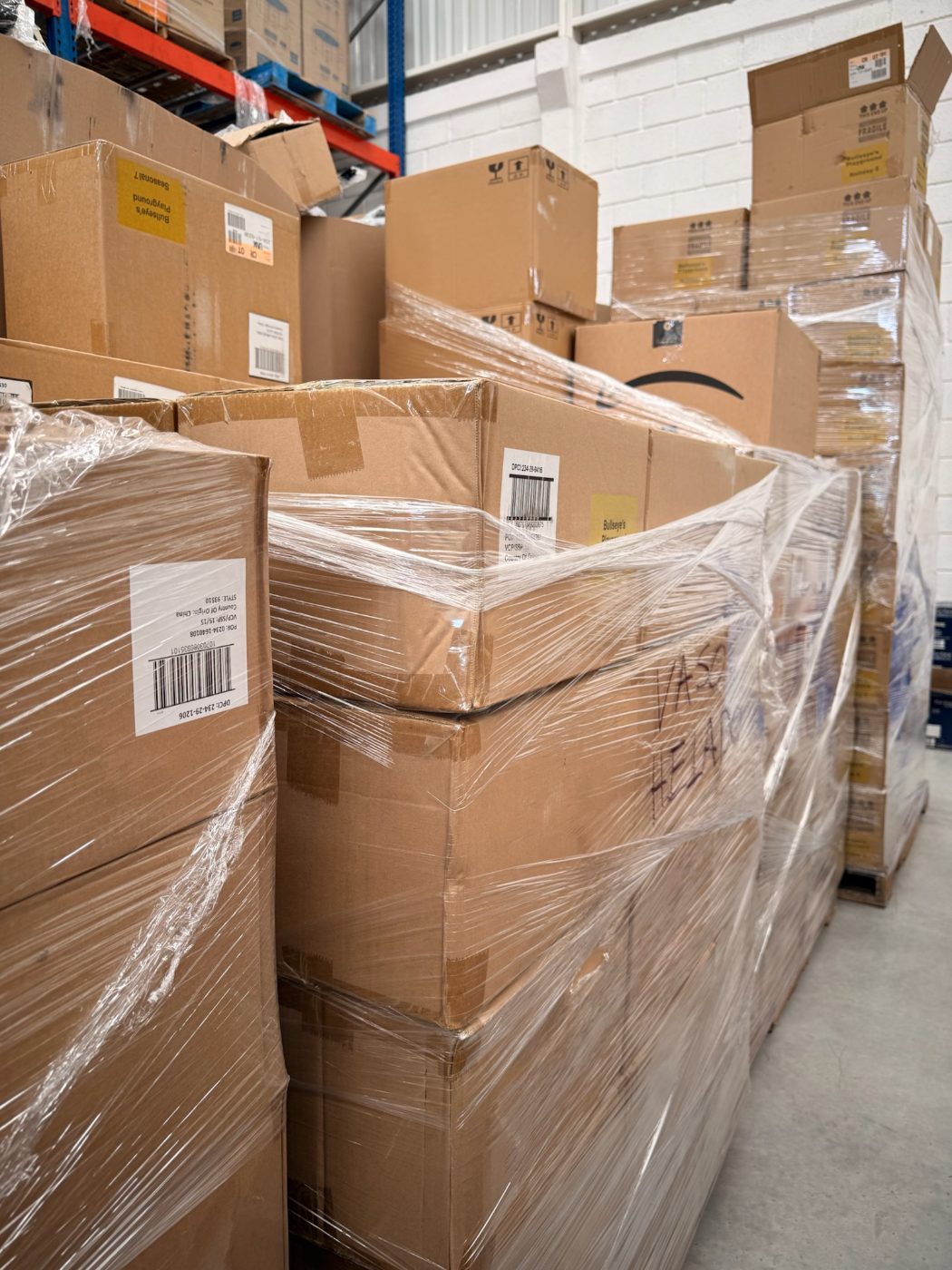 Pallets emplayados apilados contra la pared blanca de la bodega, con cajas de distintos tamaños