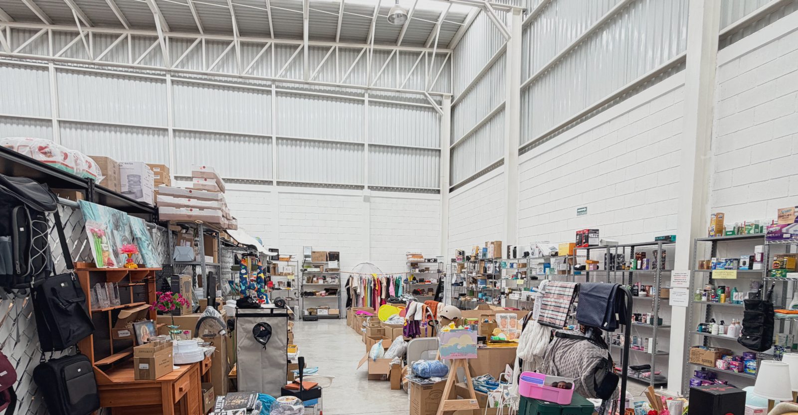 Interior de la tienda: pasillo central con anaqueles de producto a ambos lados y techo alto de nave industrial con luz de tragaluz